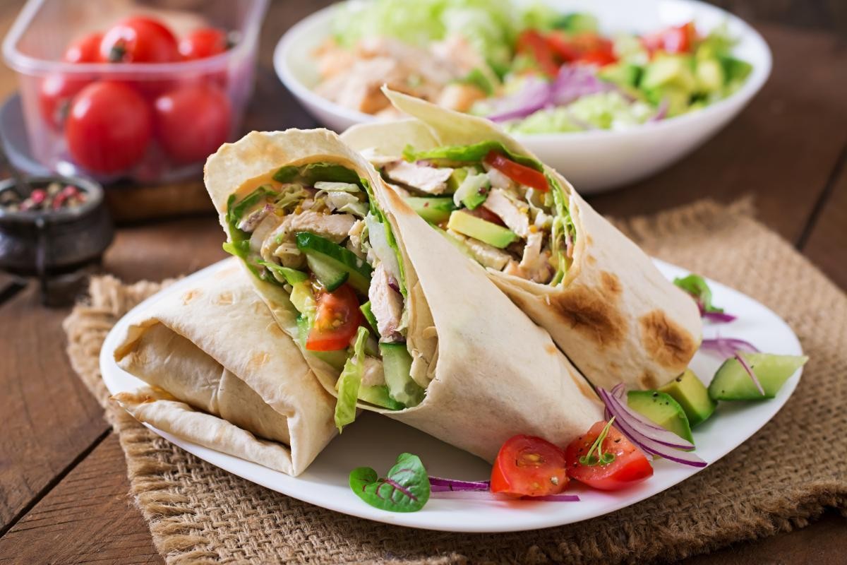 Chicken and vegetable burrito on a white plate with garnishes.