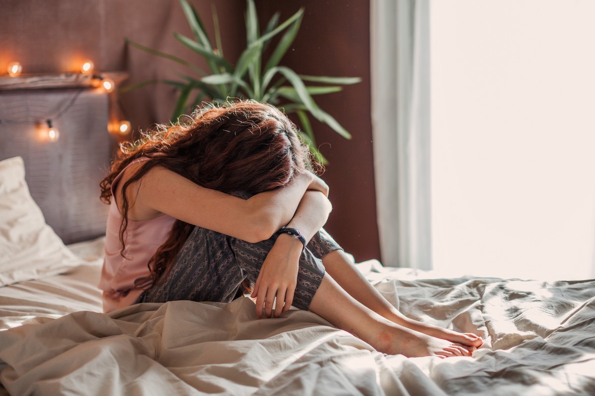 A young girl in bed, bending over with a look of sadness on her face.