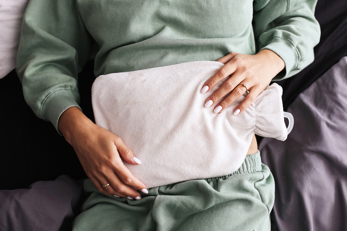 A person with a heated pad on their lower abdomen, resting in bed.