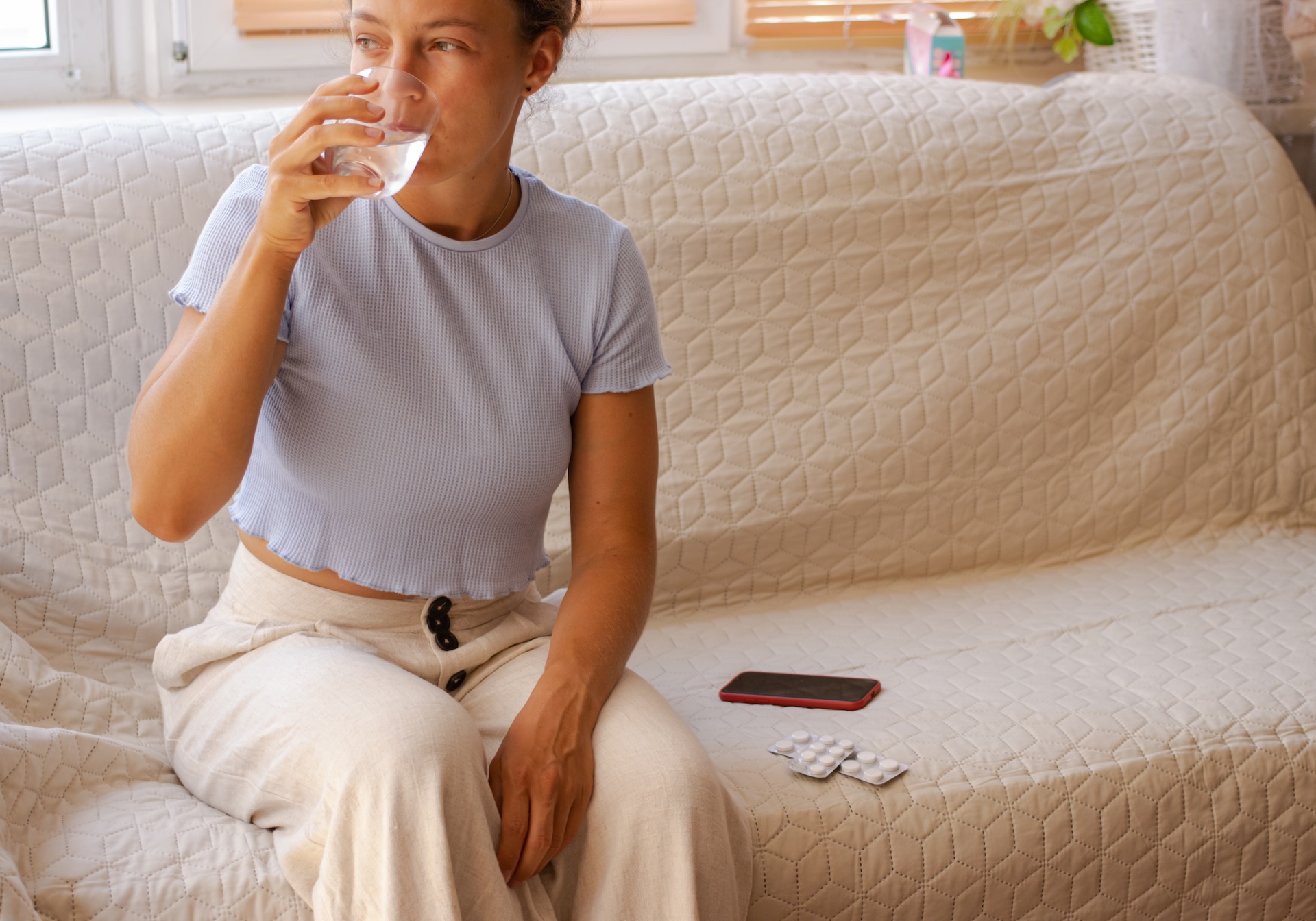 Young woman drinking water from glass, taking antibiotic painkiller pill to relieve pain.