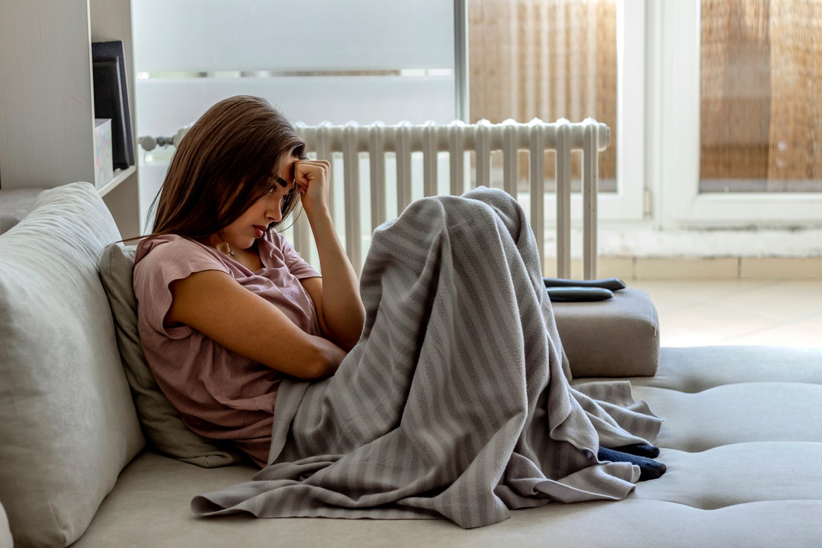 Woman sitting on a couch, holding a laptop and looking down.