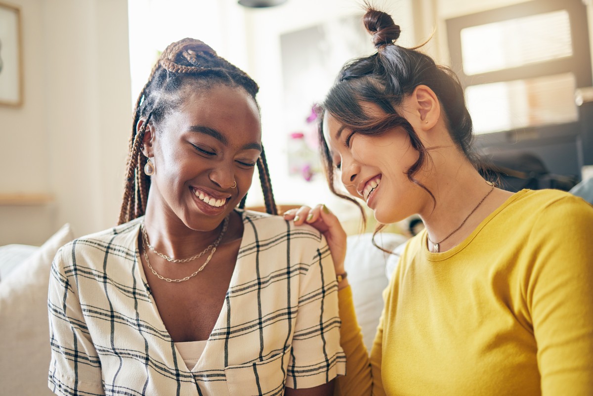 Two women conversing in a room, one with her hair in buns and the other smiling.