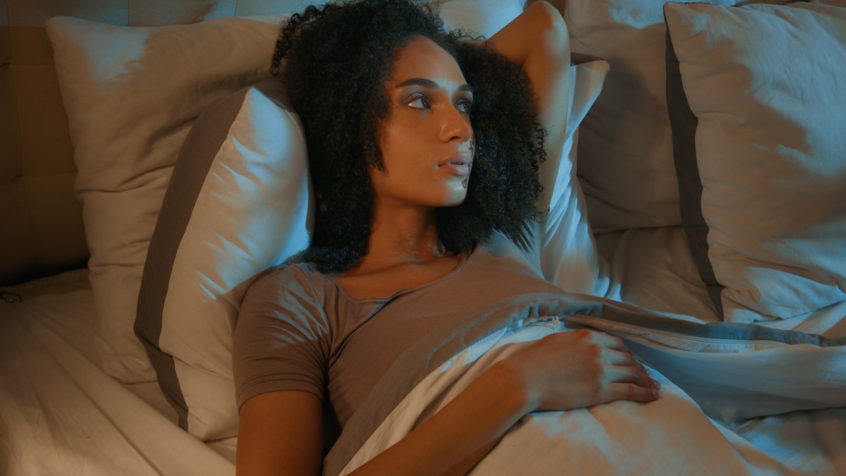 Woman lying in bed, looking to her right with a contemplative expression.