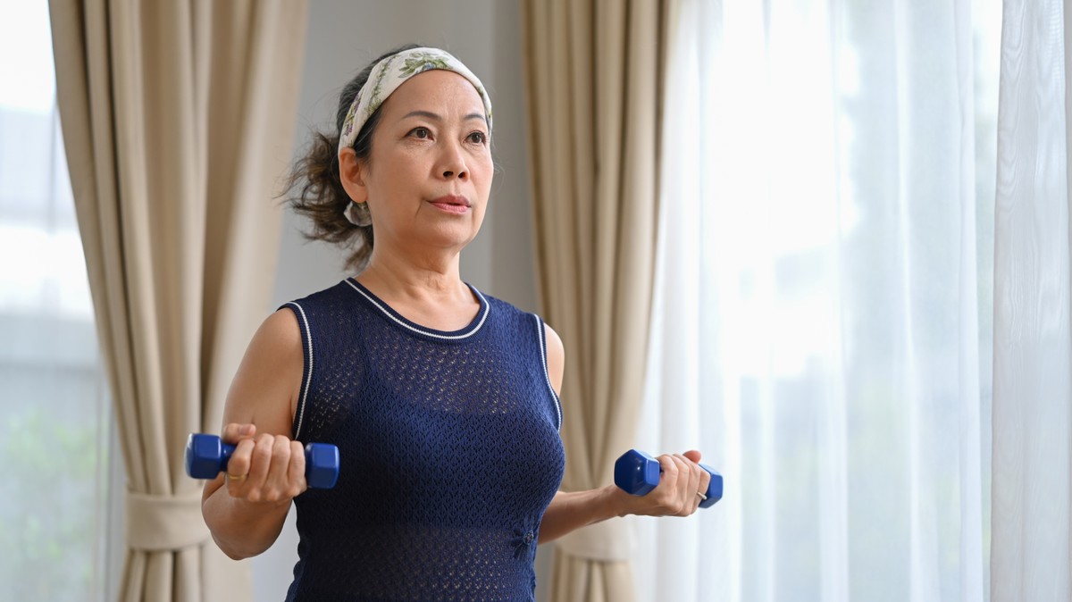 Asian woman in tank top holding a dumbbell.