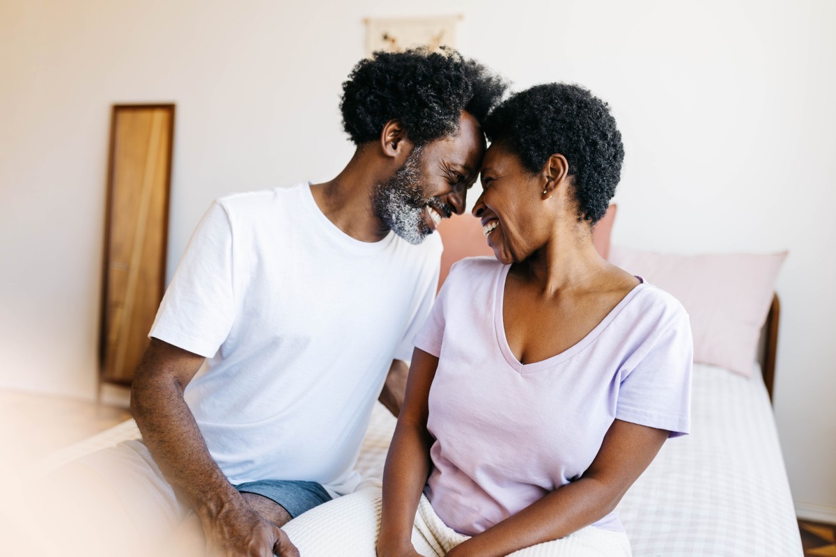Happy couple sitting on a bed, smiling and sharing an intimate moment.