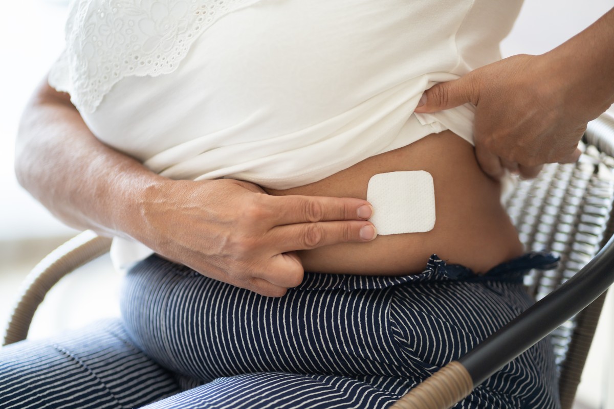 Woman in a white top applying a sticker to her abdomen.
