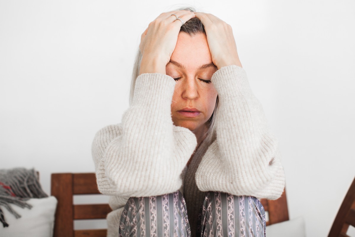 A woman with her hand on her head, wearing a white hoodie.