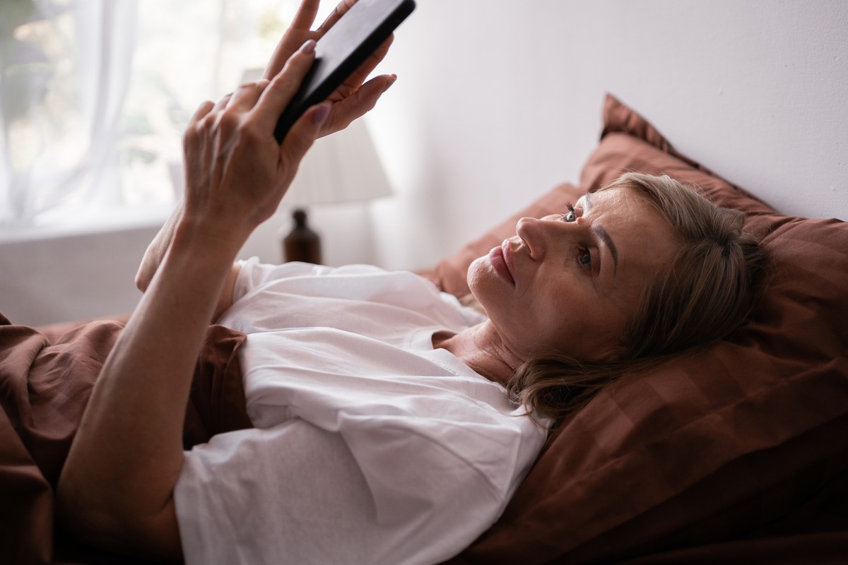 Woman lying in bed with a phone, looking at it.
