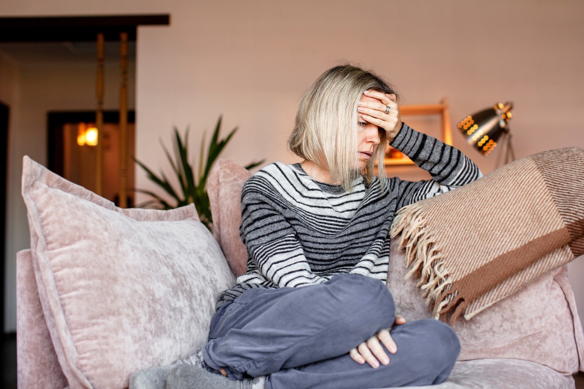 Woman seated on sofa, covering face with hand. A cozy living room scene.