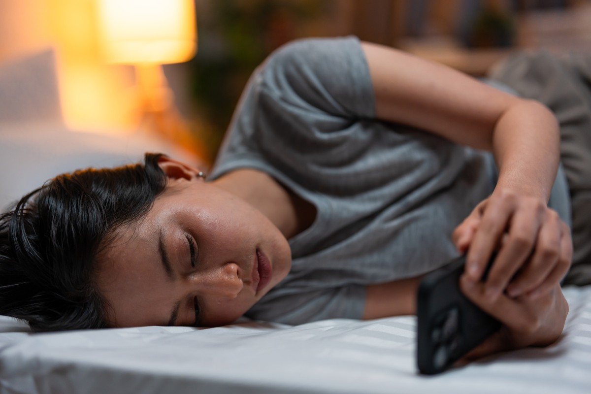 A person lying down in a bed, holding a smartphone.