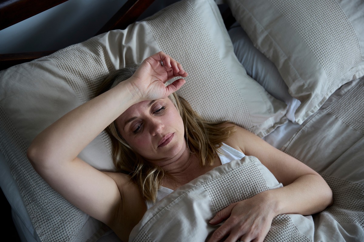 A woman resting in bed, her hand touching her forehead.