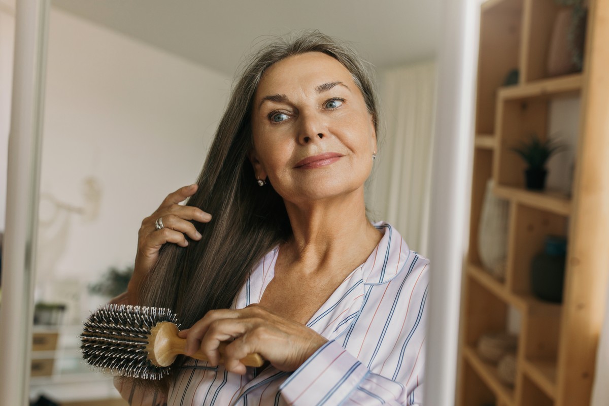 An elderly woman using a hair brush to style her hair.