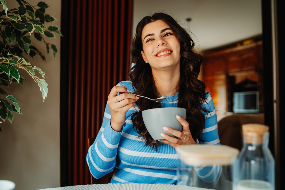 Woman seated at dining table, smiling and enjoying a meal.
