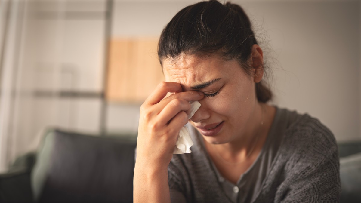 A woman touching her nose with a distraught expression.