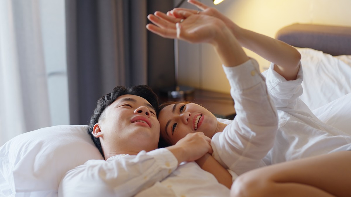 A young couple sharing a bed and smiling at the camera.