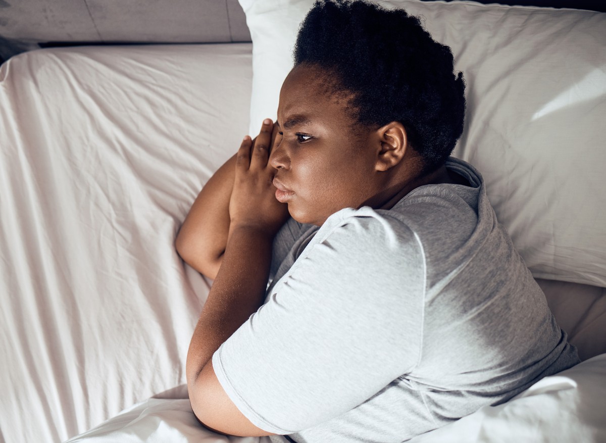 Man in bed, hands clasped over face.