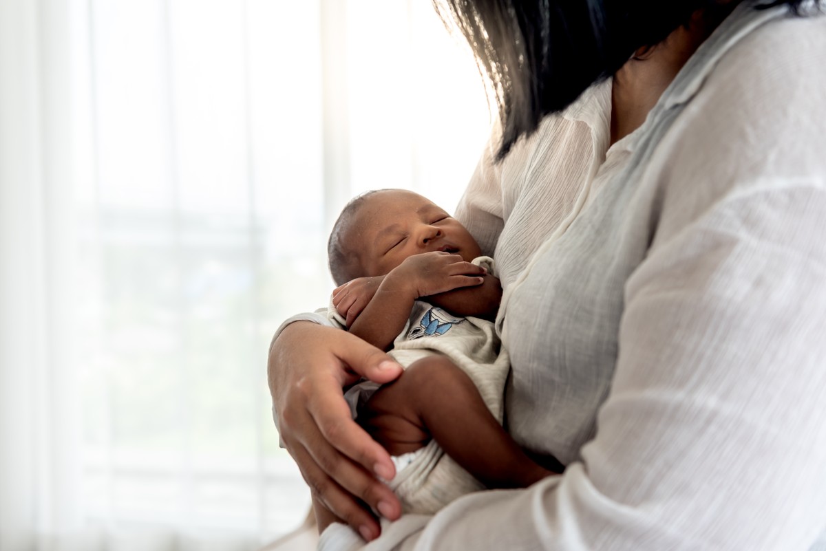 Newborn baby being held in a nursery, with caregiver holding the baby close.