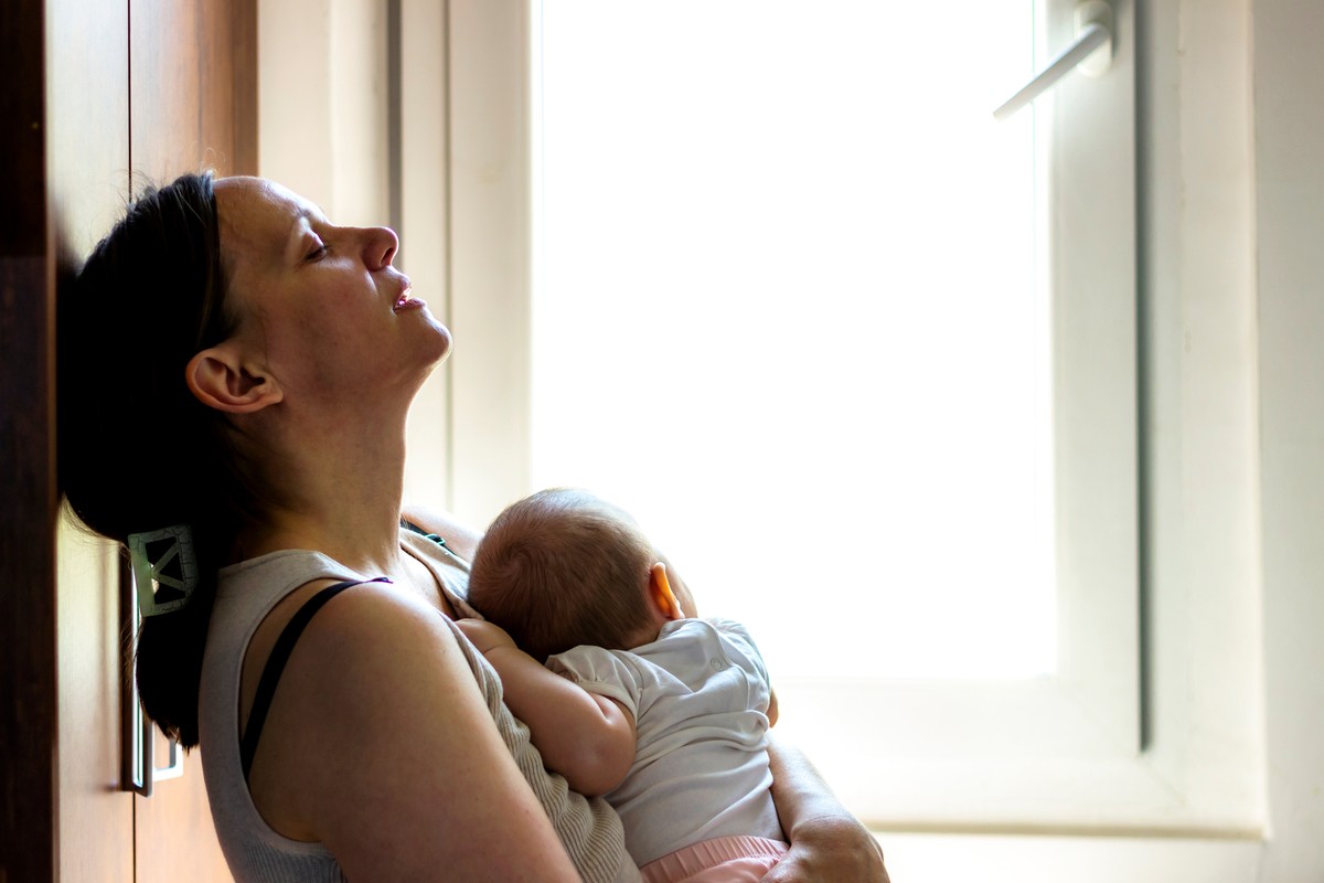Mother holding baby with gentle support, near window.