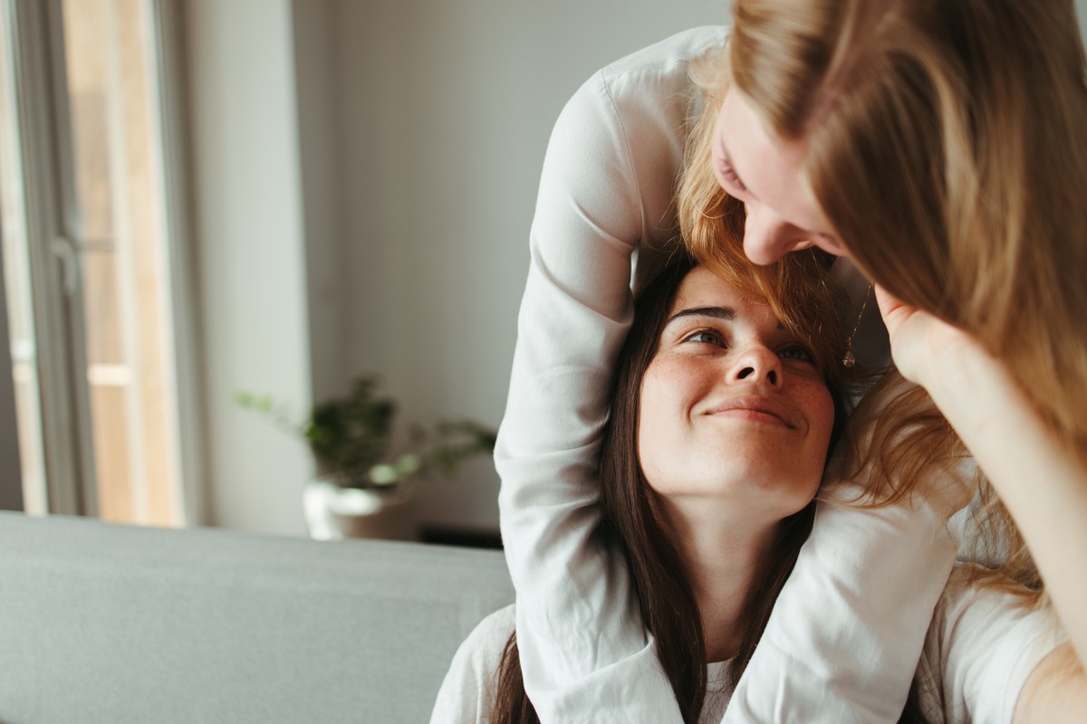 Woman playfully kissing friend's head over shoulder.