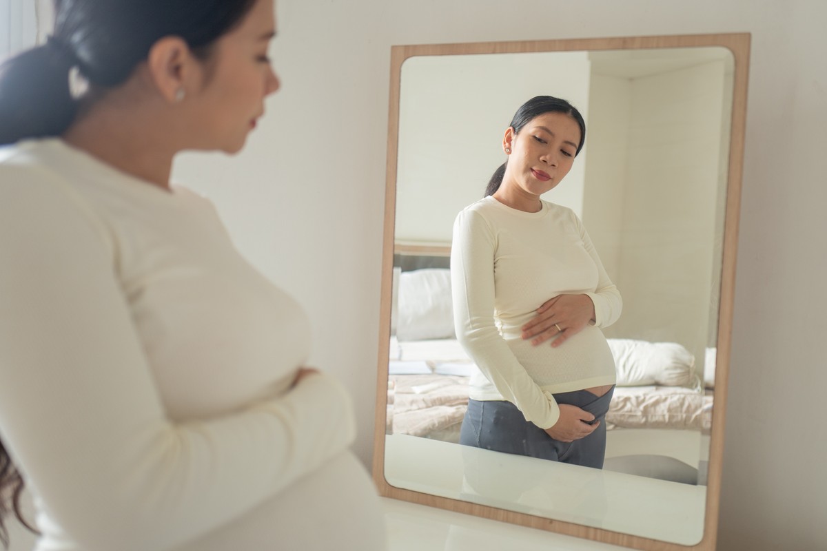 A woman, possibly pregnant, examining herself in a mirror.