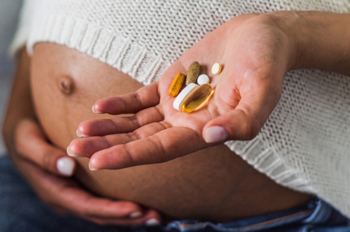 A hand holding a small bottle of supplements, with a pill inside.