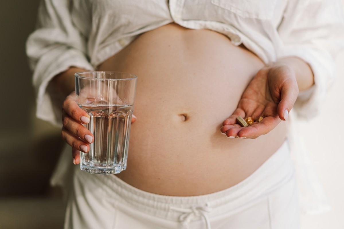 Pregnant woman with a pill in her hand, next to a glass of water.