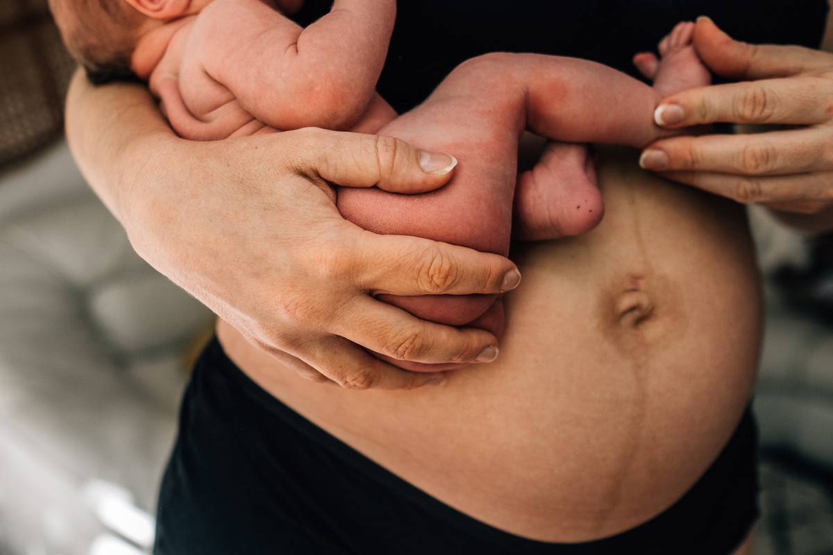 A woman cradles her belly, showing signs of labor. In the background, hands gently hold a baby.