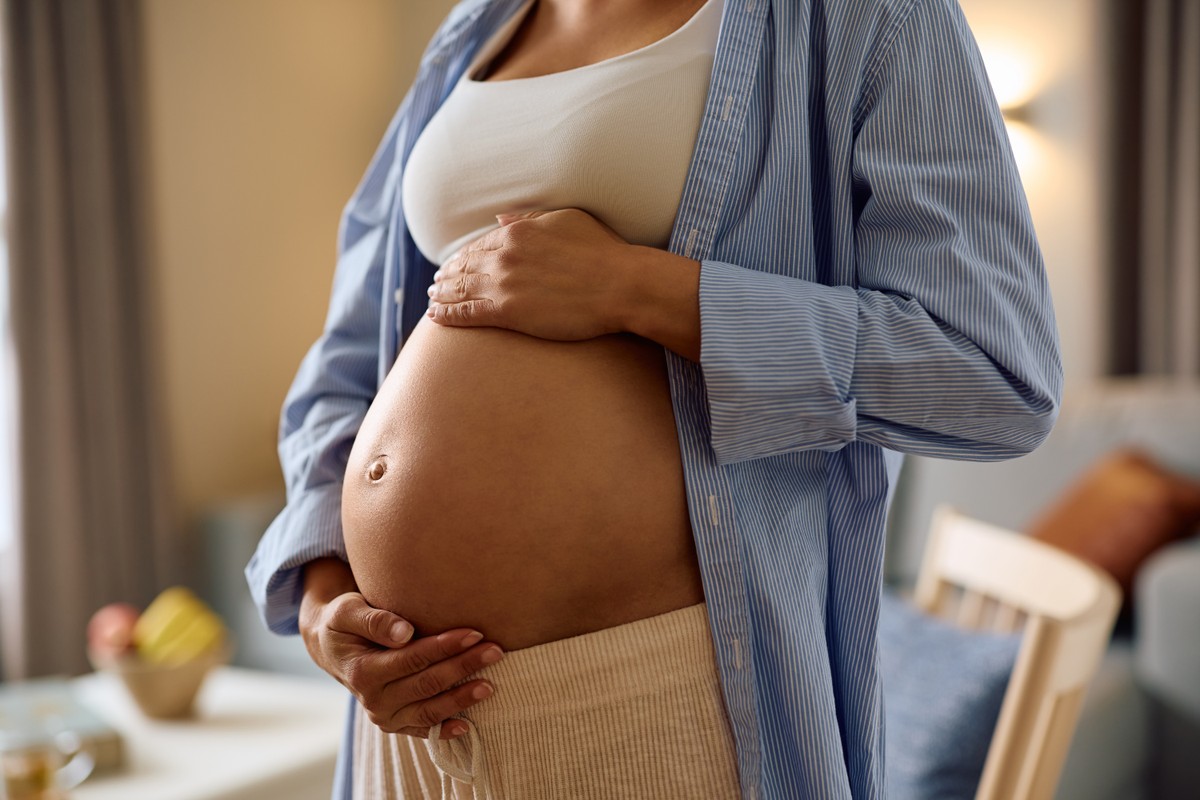 Pregnant woman in blue robe and white bra showing her belly.