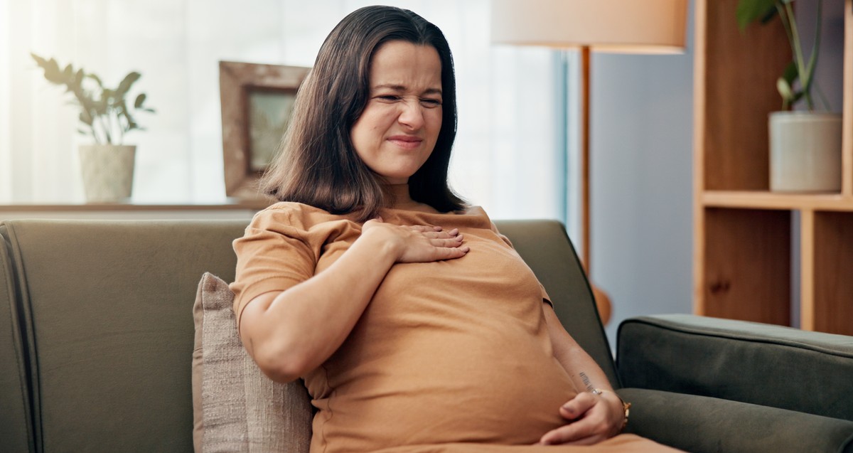 Pregnant woman sitting on a couch with her hand on her chest.