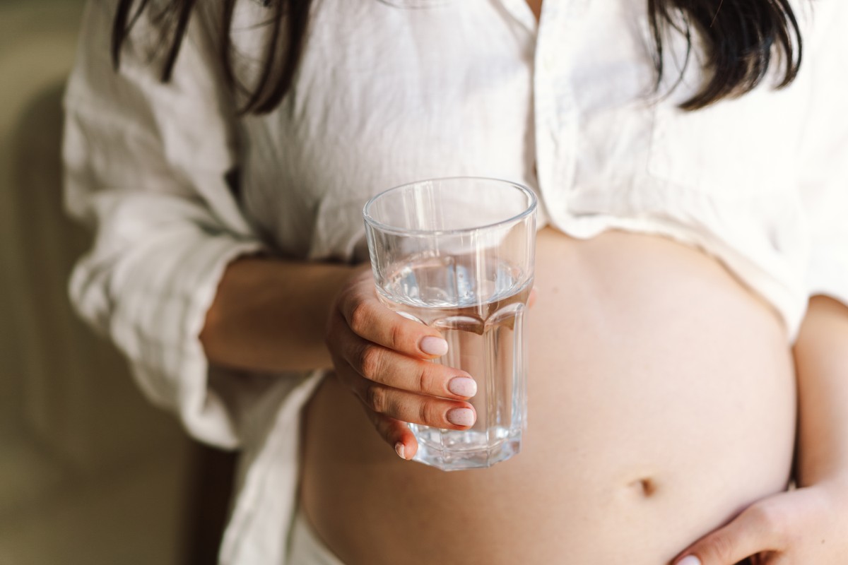 Woman holding a glass of water in her hand while wearing a white top.