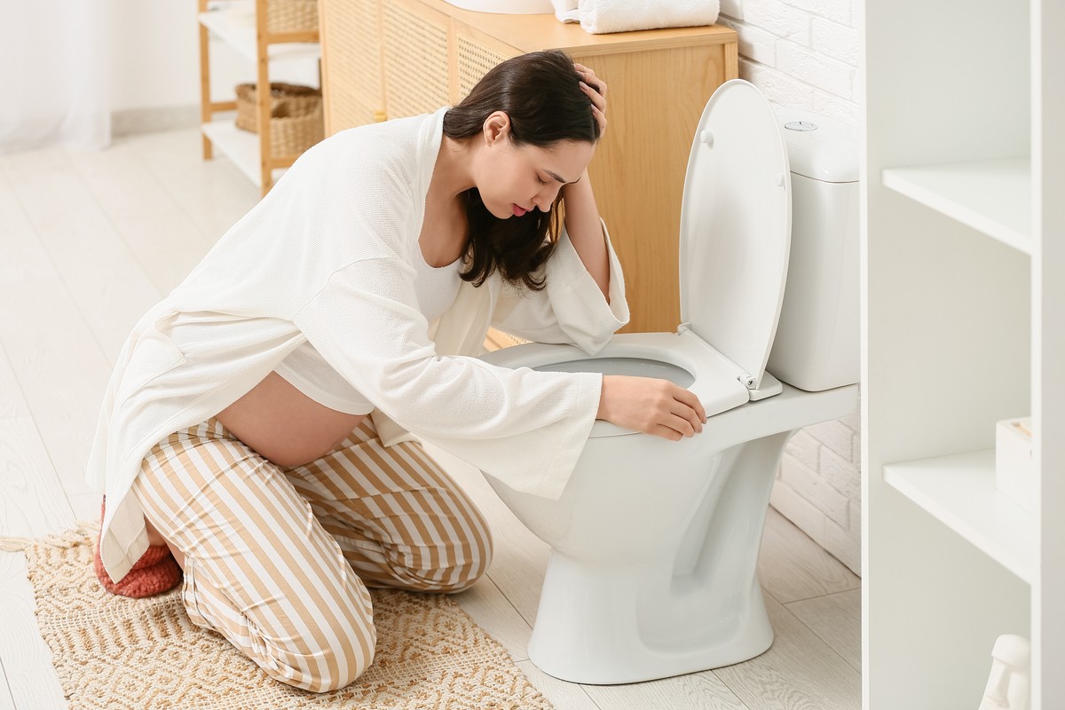 Pregnant woman touching her belly while using the toilet.