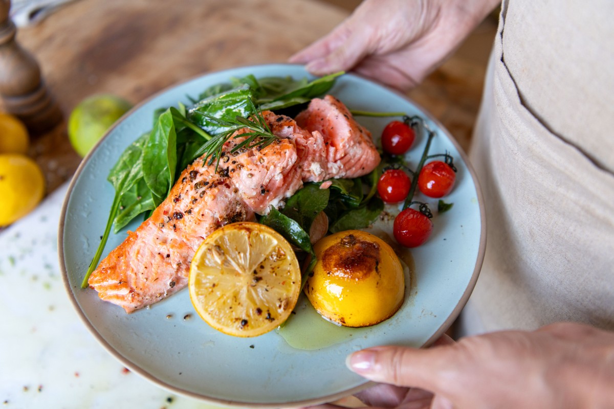 A plate of fish, salad and citrus fruits with a person holding the plate.