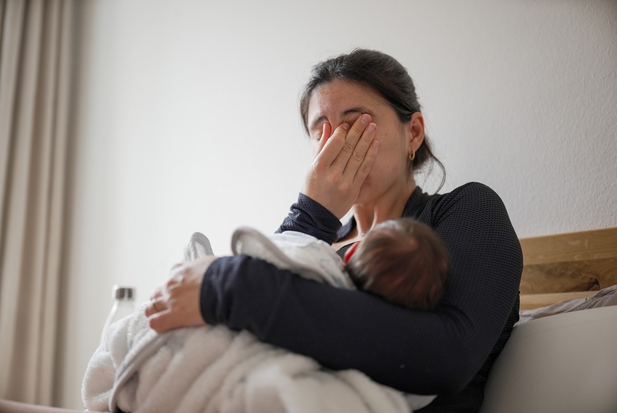 Woman in room, holding baby while crying.