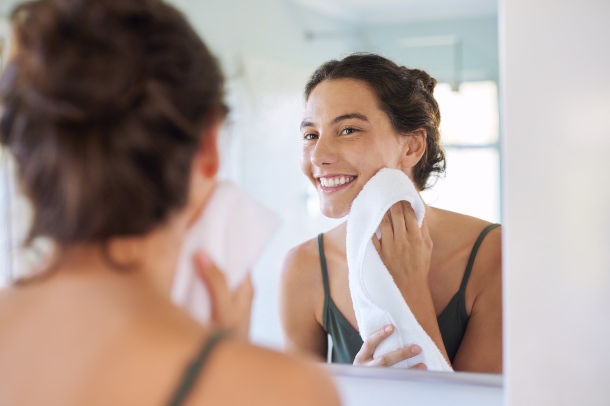 Woman smiling with towel near her face in bathroom mirror.